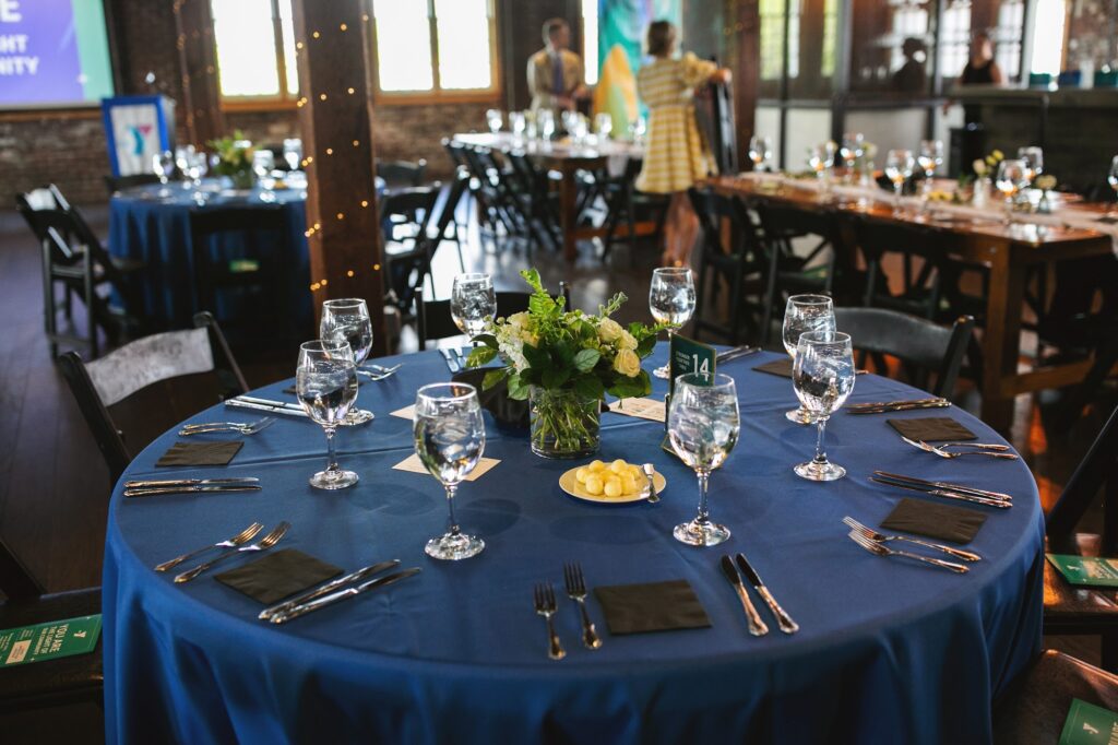 A round table dressed in navy linen with glassware and a small yellow centerpiece, ready for a corporate dinner at Tinker House