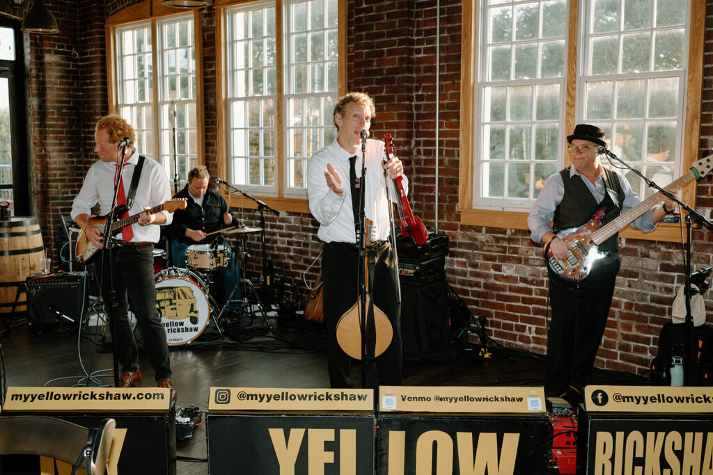 A live band playing in front of the brick wall and arched windows at Tinker House